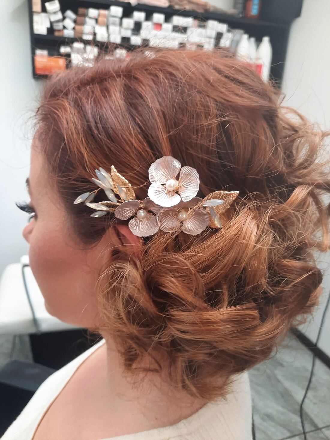 Soft, textured low updo on copper-red hair, finished with a gold and pearl floral hairpiece above the ear.